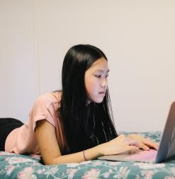 A participant lays on her bed, typing on her computer.